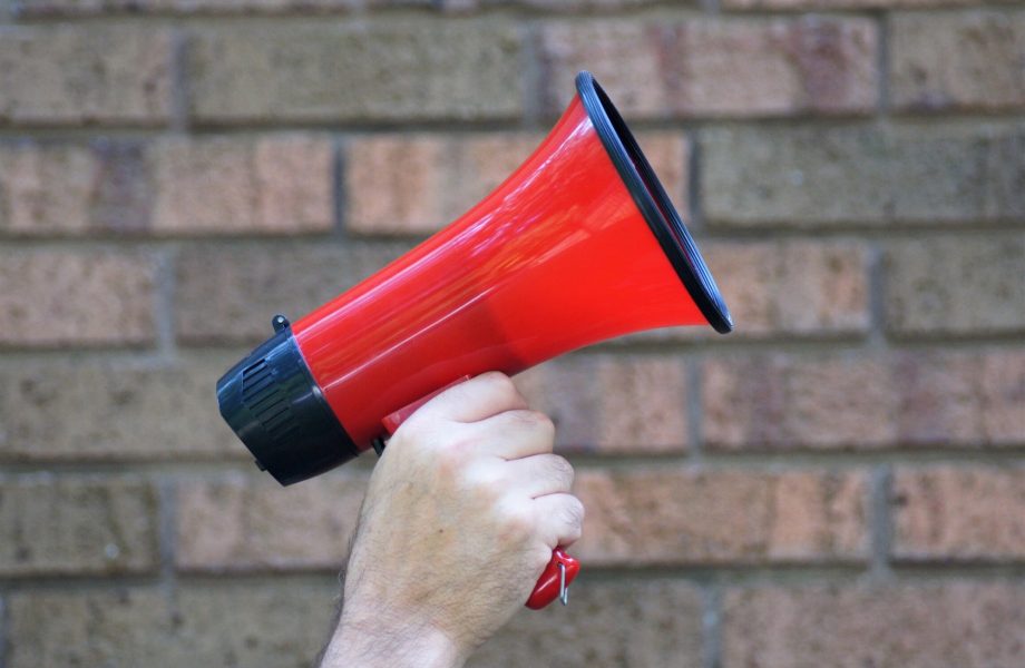 Hand holding bright red megaphone against brick wall background